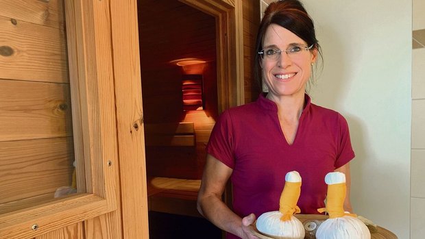 Fabienne Toppler posiert vor der Sauna, auf dem Tablett liegen Kräuter- und Blütenstempel für ihre Wellnessbehandlungen parat.