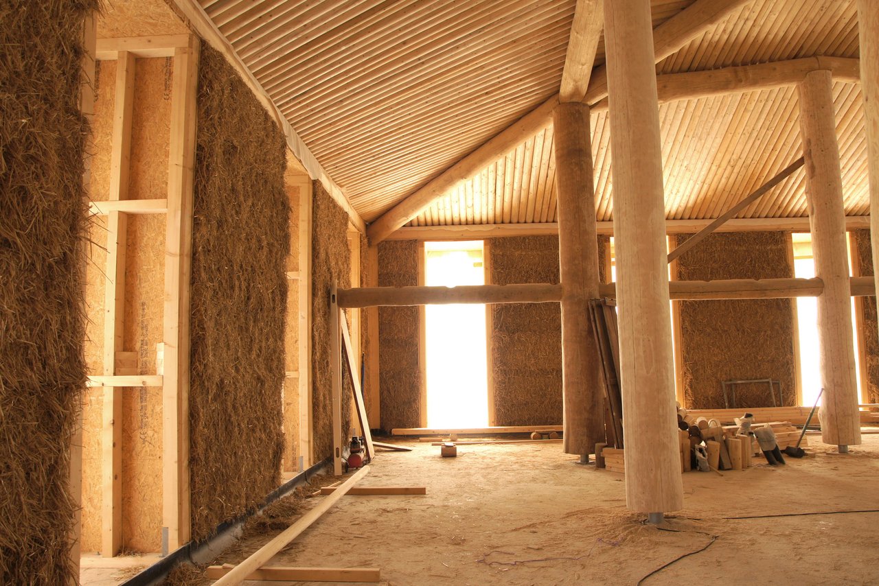 Ein Strohballenhaus – hier mit lasttragenden Holzstammstützen – von innen. Die Wände werden mit Lehm verputzt. (Bild Atelier Schmidt)