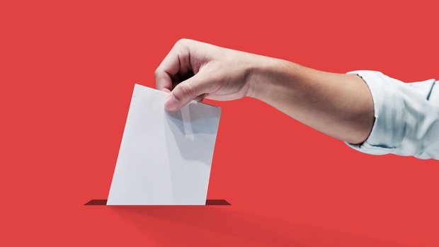 Symbolbild einer Hand, welche einen Stimmzettel in die Urne wirft.