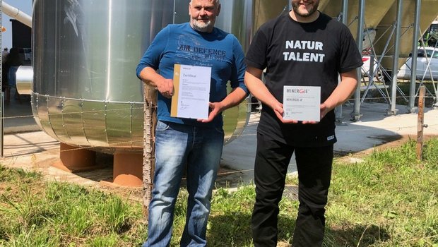 Die Landwirte Hans (links) und Mathias Leuenberger mit den Minergie-A-Zertifikaten, die seit diesem Sommer den Technikraum und die Fassade ihrer klimaneutralen Geflügelmasthalle zieren. (Bild jw)