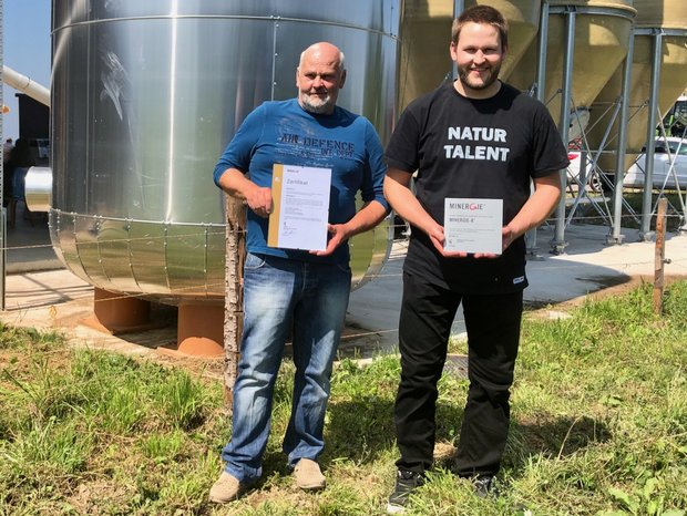 Die Landwirte Hans (links) und Mathias Leuenberger mit den Minergie-A-Zertifikaten, die seit diesem Sommer den Technikraum und die Fassade ihrer klimaneutralen Geflügelmasthalle zieren. (Bild jw)