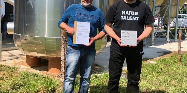 Die Landwirte Hans (links) und Mathias Leuenberger mit den Minergie-A-Zertifikaten, die seit diesem Sommer den Technikraum und die Fassade ihrer klimaneutralen Geflügelmasthalle zieren. (Bild jw)