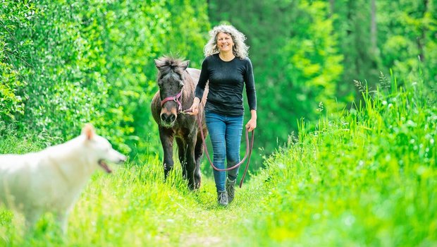 Neben einer der Hecken, die zum Betrieb gehören, spaziert Corinne Kählin mit ihrer alten Stute Dögg. Im Vordergrund die Hündin Dis, eine der sieben Hunde, die auf dem Hof alt werden dürfen.