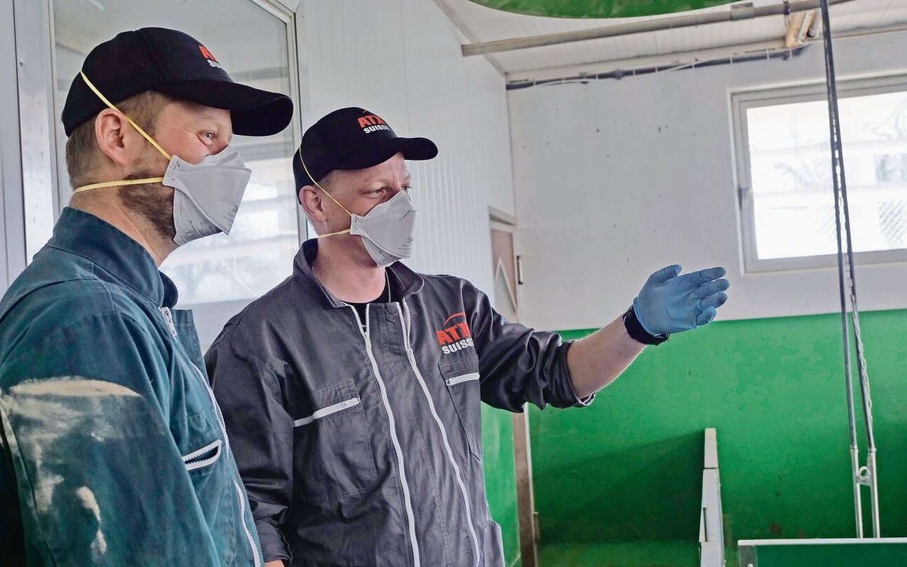 Brian Dähler (links) und Patrick Bucher diskutieren miteinander. Sie tragen im Stall Maske, Handschuhe und Kombi.