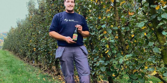 Michael Budliger in der Anlage mit den abgeernteten Säulenbäumen und einer Flasche seines «Suure Moscht». Die Mostobsthecke hat einen Baumabstand von bloss 50 Zentimetern.