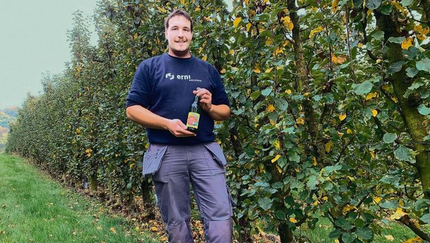 Michael Budliger in der Anlage mit den abgeernteten Säulenbäumen und einer Flasche seines «Suure Moscht». Die Mostobsthecke hat einen Baumabstand von bloss 50 Zentimetern.