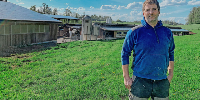  Philipp Boss von der Büelweid in Knonau vor den Gebäuden mit PV-Anlagen. Links die Maschinenhalle, rechts die Milchviehscheune, hinten die überdachten Fahrsilos. Nicht sichtbar ist die ebenfalls mit PV-Modulen belegte Geflügelmasthalle. 