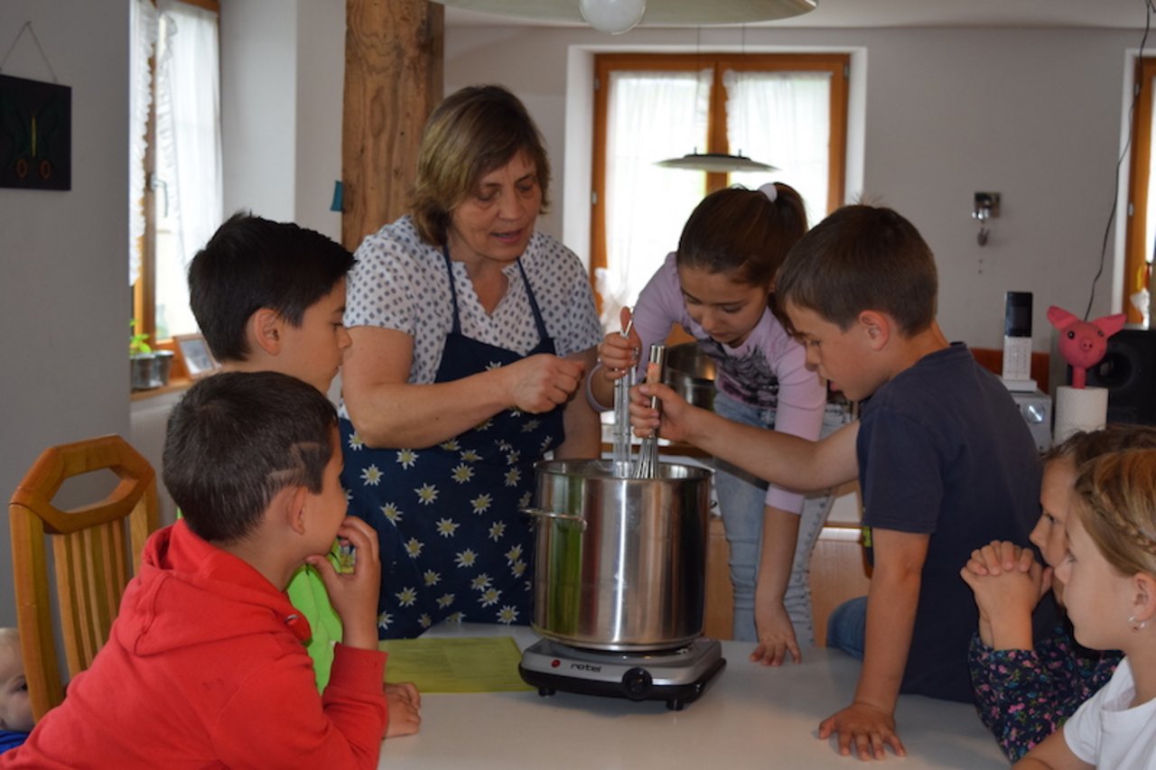 Käthi Vetterli erklärt den Kindern, was mit der Milch durch die Zugabe von Lab geschieht. (Bild sgi)