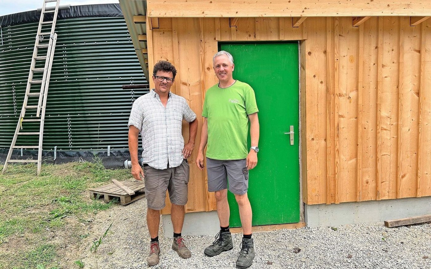 Rolf Mengelt und Andreas Braun (v. l.) stehen vor dem Pumpenhäuschen. Hinter ihnen ist ihr grünes Wasserreservoir zu sehen, das von Grundwasser gespeist wird. Von dort wird das Wasser in ihre Felder geleitet.
