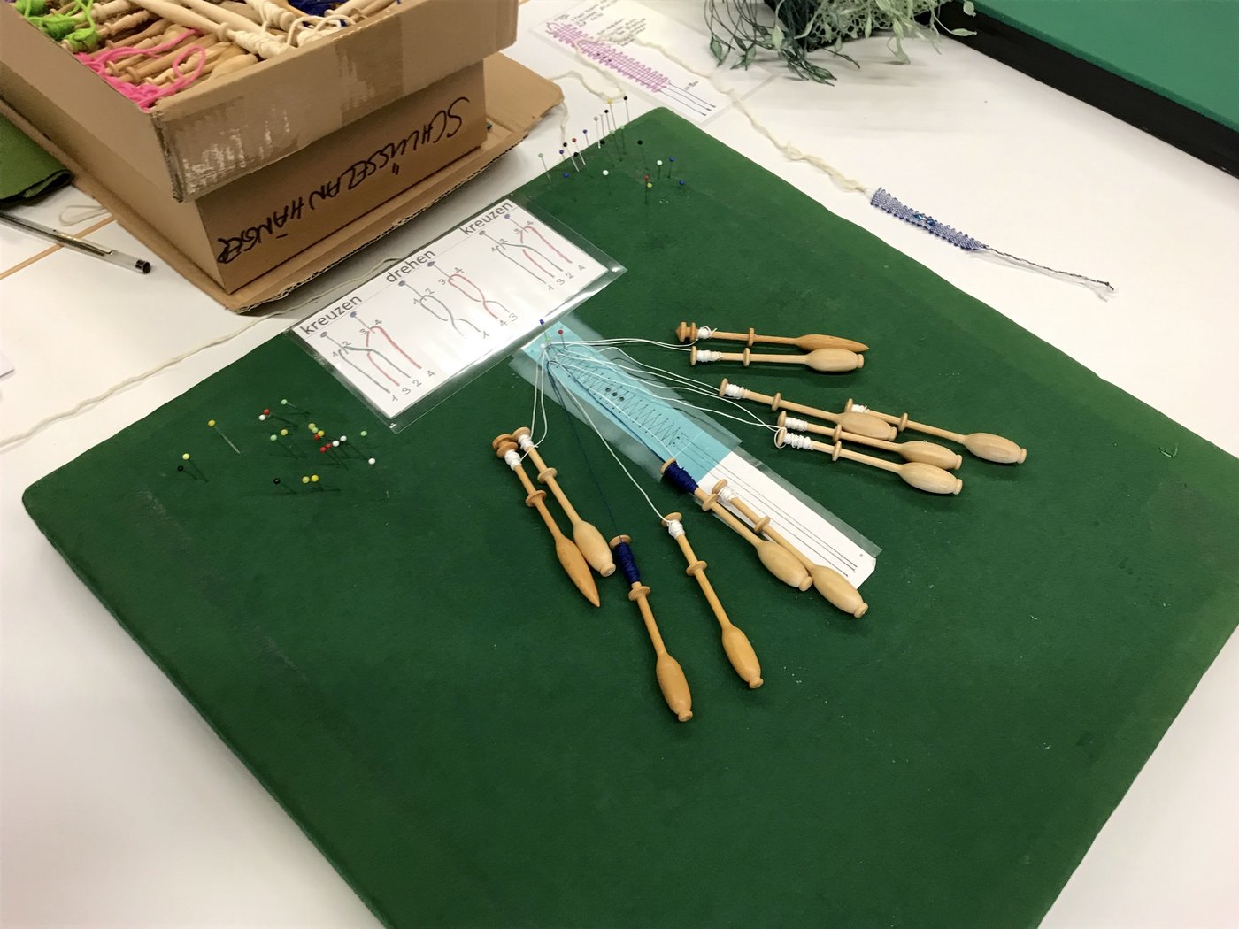 Das sind die Klöppelutensilien: Das Klöppelkissen, die Klöppel aus Holz, um welche die Fäden gewickelt sind, sowie Stecknadeln zum Befestigen.