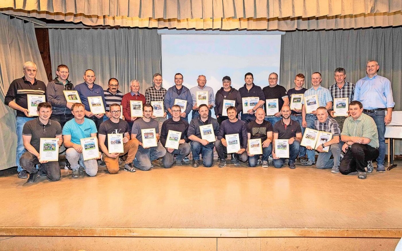 Martin Rust von Braunvieh Schweiz (hinten rechts) und Präsident Roland Disler  (vorne rechts) mit den 25 ausgezeichneten Besitzern der 100 000er-Kühe.