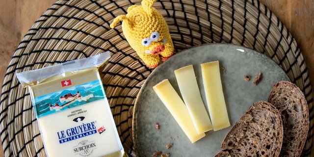 Das gestrickte Migros-Maskottchen posiert vor Käse, der beim Detailhändler nun günstiger zu haben ist. (Bild Migros)