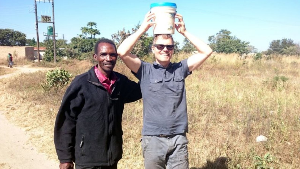 Der „Headman“ (so etwas wie ein traditioneller Gemeindepräsident) und der „Muzungu“ (Bezeichnung für einen Weissen) in Mphango. Ich übe mich im Milchkesseltragen auf dem Kopf, kann aber den sambischen Frauen nicht annähernd das Wasser reichen. (Bilder Markus Schär/zVg)