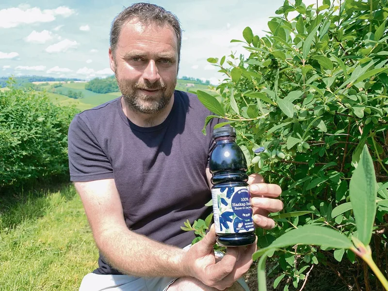 Thomas Joss präsentiert in der Anlage mit Haskap-Beerensträuchern eines der Produkte daraus, den Bio-Direktsaft.