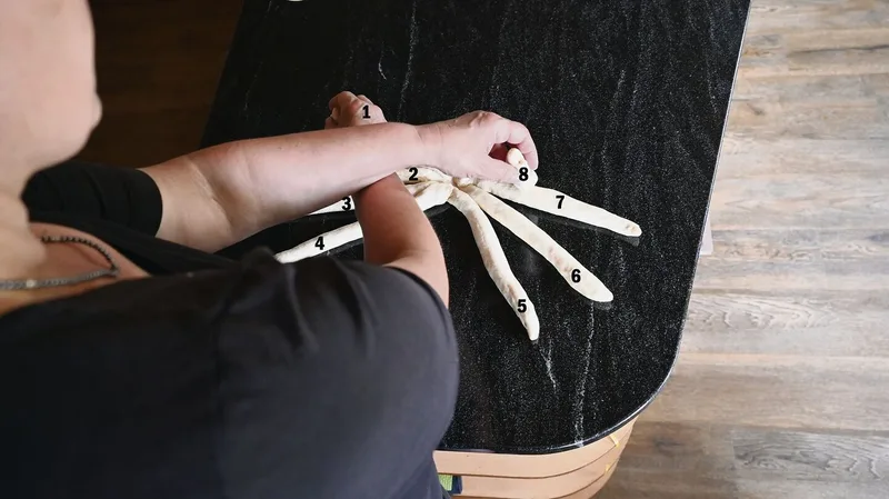 Mit der rechten Hand Strang 1 nehmen, die linke Hand nimmt Strang 8, Stränge kreuzen.