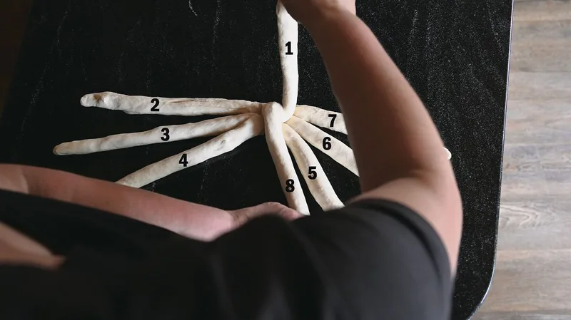 Die linke Hand legt den Strang neben Strang 5, die rechte behält Strang 1 in der Hand.