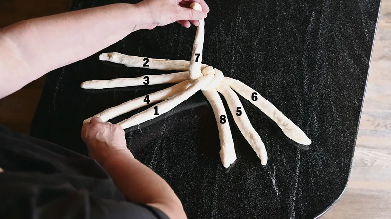 Mit der linken Hand Strang 7 holen, kreuzen. Rechte Hand legt Strang 1 neben Strang 4, die linke behält Strang 7 in der Hand.
