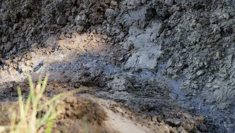 Ein dünnes Wasserrinnsal fliesst durch lehmigen Boden.