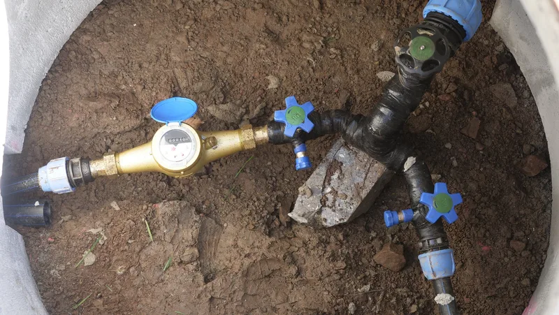 Blick von oben in einen Schacht: Von einer Leitung zweigen zwei ab, eine mit einer Wasseruhr versehen.