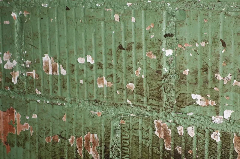 Eine grüne Stallwand, von der die Farbe abblättert.