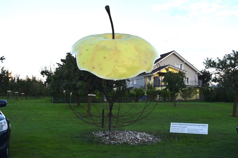 Ein grosser Apfel aus Drahgeflecht steht am Rande der Obstparzelle und heisst die Besucher willkommen.