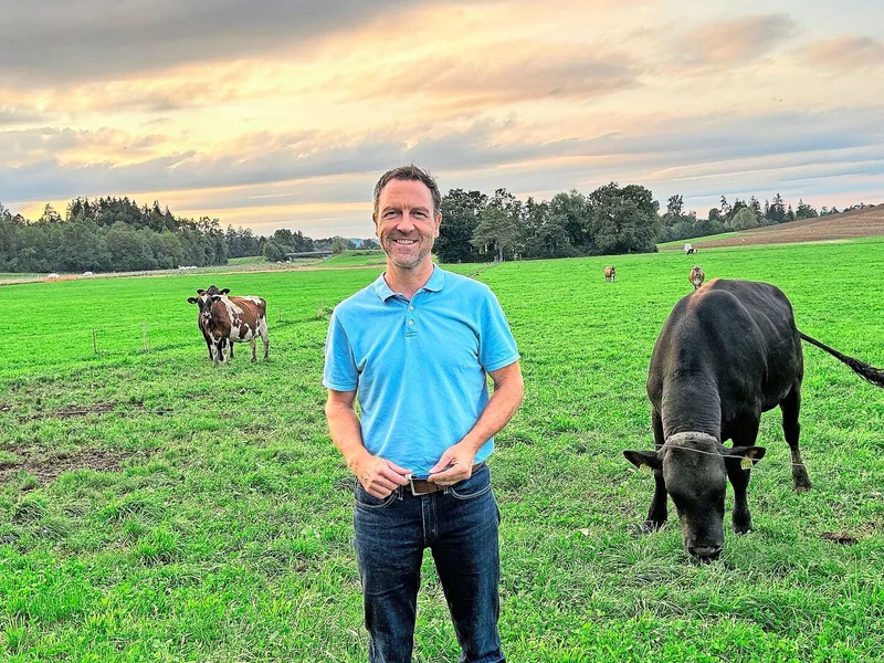 Hinter Daniel Nyfeler ist die Weide mit Stier Ando zu sehen. Der Stier sorgt für Fruchtbarkeit in den heissen Sommermonaten.