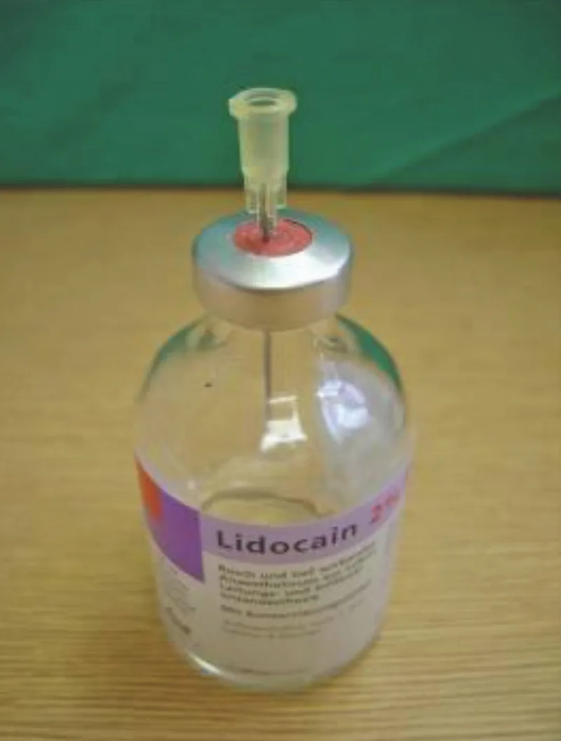 Eine Flasche des Lokalanästhetikums Lidocain, in welcher eine Spritzenspitze im Gummi steckt.