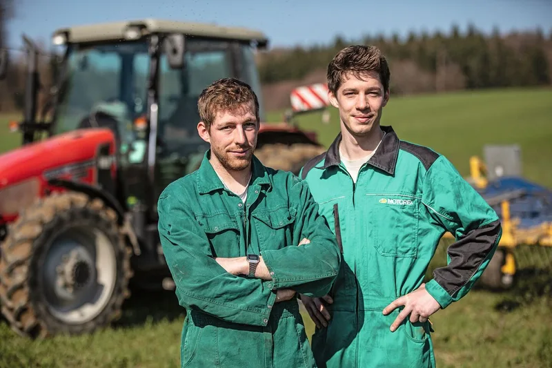 Die Brüder Ramseyer stehen im Overall vor dem Traktor auf dem Feld.