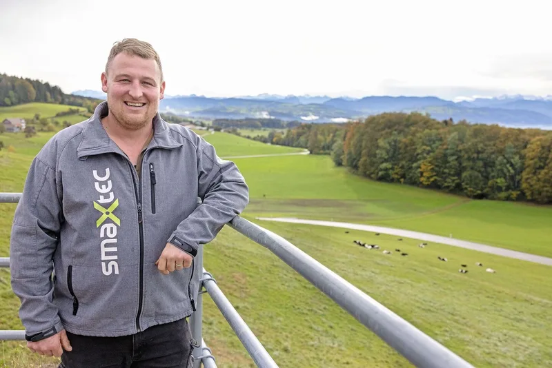 Tobias Wehnert lehnt sich an die Metallstangen im Laufhof. Hinter ihm ist die Kuhweide zu sehen.