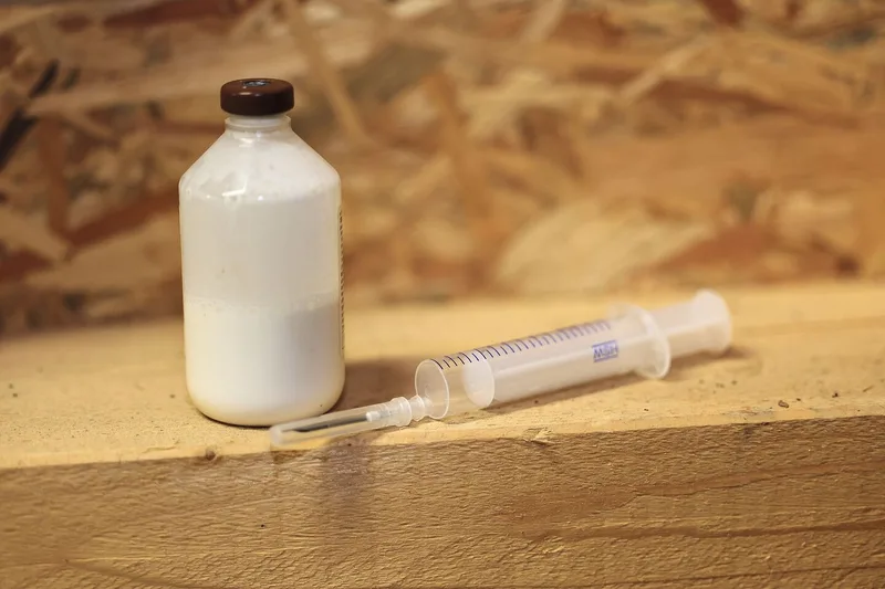Eine Glasflasche, gefüllt mit einer milchigen Substanz, daneben liegt eine leere Spritze.