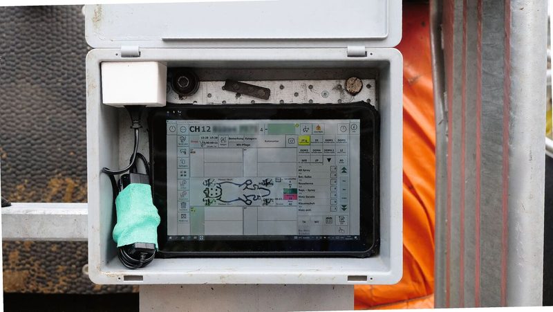 Ein Tablet steht in einer grauen Kiste, die am Klauenstand montiert ist. Auf dem Display sieht man die Daten der aktuell zu behandelnden Kuh.