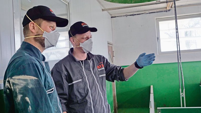 Brian Dähler (links) und Patrick Bucher diskutieren miteinander. Sie tragen im Stall Maske, Handschuhe und Kombi.