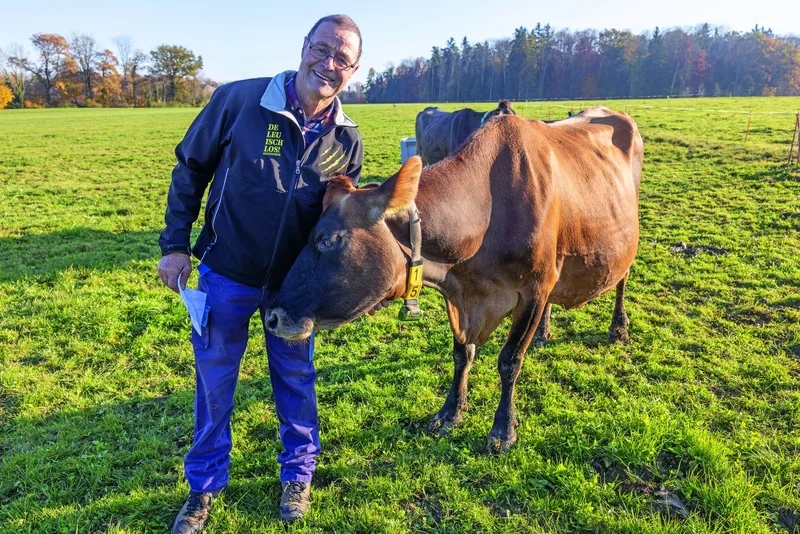 Ruedi Rutishauser steht auf der Weide und krault der Kuh den Hals.